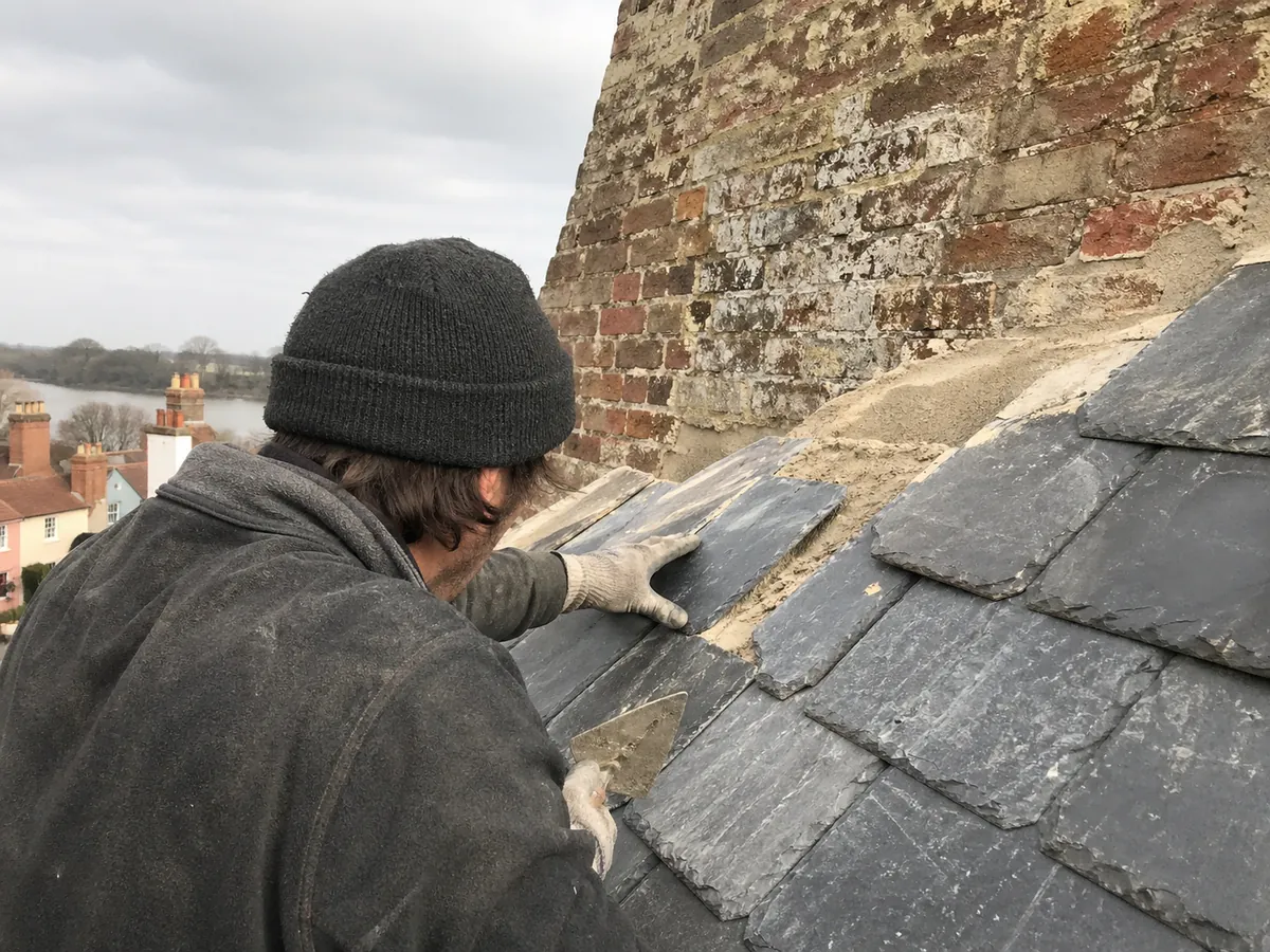 Roofer bedding natural slates against a chimney on a Woodbridge period property overlooking the Deben